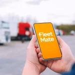 Hand holding smartphone with Fleet Mate app logo in fleet yard – Mobile command & control for GPS tracking Brisbane, Australia