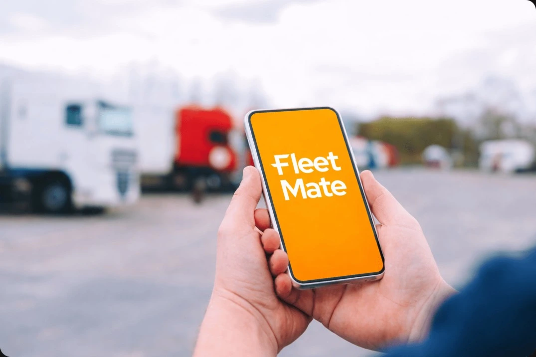Hand holding smartphone with Fleet Mate app logo in fleet yard – Mobile command & control for GPS tracking Brisbane, Australia